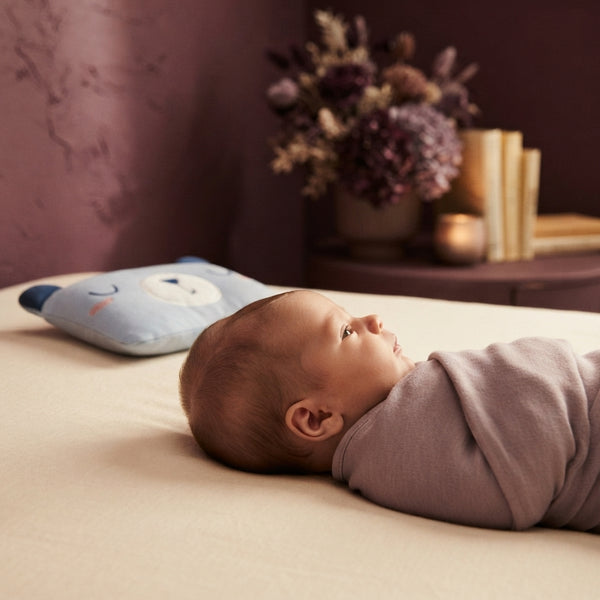 Close-up view of a newborn baby lying on a bed with a focus on their head position in a soft, cream-toned nursery environment