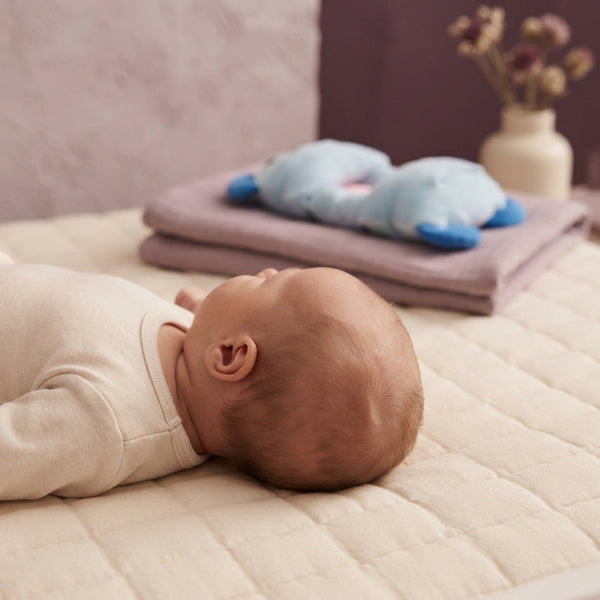 Close-up of a newborn baby on a mattress highlighting the need for head shape support with a soft textile backdrop in lilac a